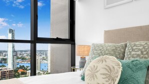 Hotellihuone, jossa on suuri ikkuna, kuviollisilla tyynyillä varustettu sänky, yöpöytälamppu ja näkymä kaupungin siluettiin.