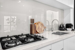 Eine moderne Küche mit Gasherd, Edelstahlspüle und Schneidebrett aus Holz.