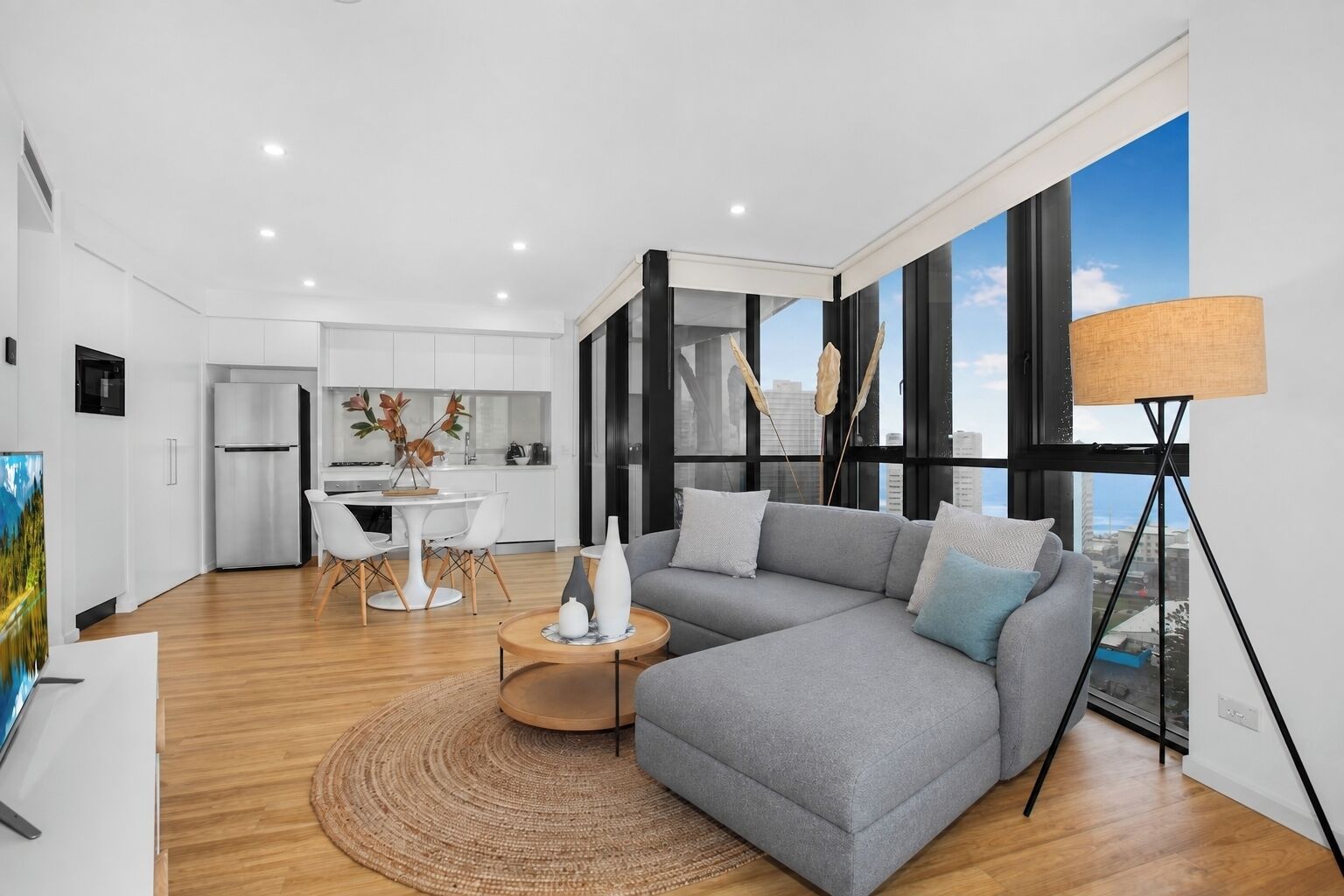 A modern living room with a grey sectional sofa, a round coffee table, and a large window with a view of the city.