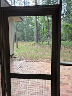 Vista a través de una puerta que muestra un patio empedrado con césped y árboles.