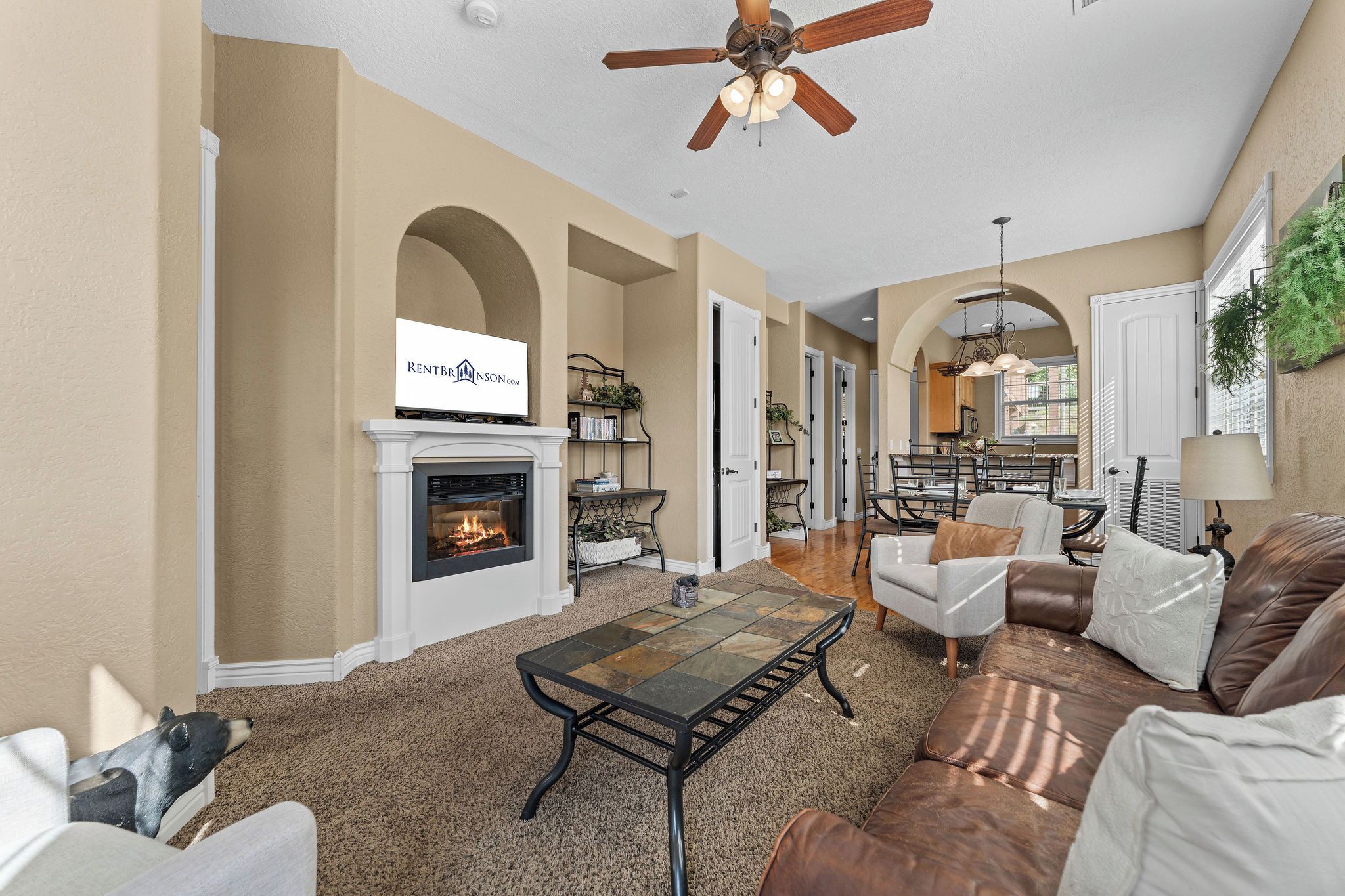 A spacious living room with a fireplace, a dining area, and a kitchen visible through an archway.