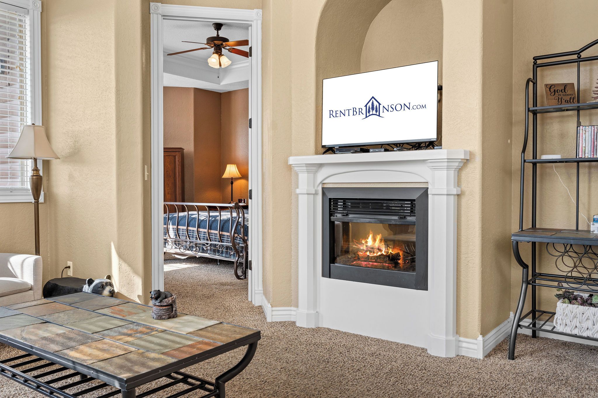 A living room with a fireplace, a television mounted above it, a bookshelf, and a dog bed with a dog.