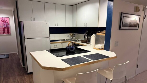 A compact kitchen with white cabinets, a built-in stove, and a small island with bar stools.