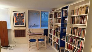 A room with a desk, chairs, a bookshelf, and a window with blinds.