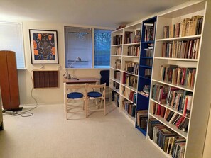 Ein Zimmer mit Schreibtisch, Stühlen, einem Bücherregal und einem Fenster mit Jalousien.