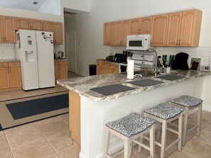 A kitchen with wooden cabinets, a white refrigerator, a microwave, a stove, and a bar area with stools. - Privacy, pool and close to Manasota Beach (Englewood)