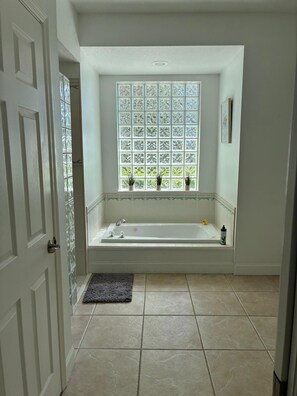 Ein Badezimmer mit Badewanne, einem Fenster mit Dekorationsglas und einer Tür.