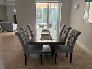 A dining area with a long table, six upholstered chairs, and a view through a sliding glass door. - Privacy, pool and close to Manasota Beach (Englewood)