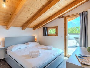 Une chambre avec un plafond en bois, un lit recouvert de draps blancs, une petite fenêtre et une vue sur l’extérieur.