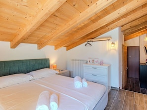 A bedroom with a wooden ceiling, a bed with white linens, a nightstand, and a dresser with drawers. - Apartment Olivo by Interhome (Sorico Albonico)