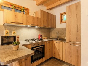 A kitchen with wooden cabinets, a gas stove, a microwave, and a sink. - Apartment Olivo by Interhome (Sorico Albonico)