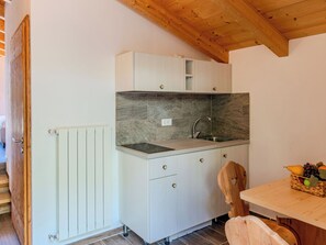 A compact kitchen with a built-in sink, a wooden ceiling, and a dining area with a fruit basket. - Apartment Olivo by Interhome (Sorico Albonico)