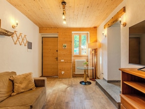 A cozy room with a wooden ceiling, a glass table, a sofa, and a TV on a wooden stand. - La Palma by Interhome (Sorico Albonico)