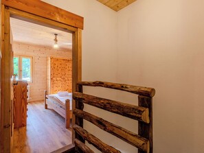 Un interior de madera con una cama, un banco de madera y una puerta que da a otra habitación.