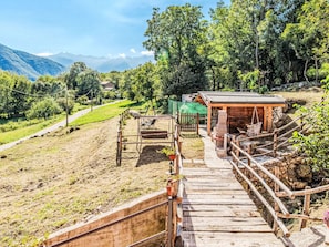 A wooden staircase leading to a rustic wooden structure with a metal railing, surrounded by a grassy area and trees. - La Palma by Interhome (Sorico Albonico)