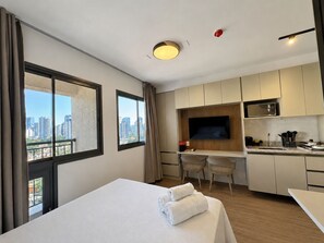 Ein Hotelzimmer mit Bett, Schreibtisch, Küchenzeile und Fernseher.