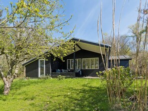 Eine Hütte mit Veranda, großen Fenstern und einem geneigten Dach.