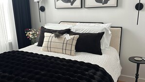 Camera da letto ordinata con un letto, cuscini, una coperta nera, un vaso con fiori e due lampade a parete.