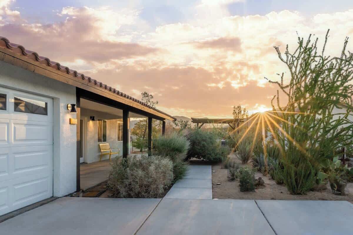 Una casa moderna con porche cubierto, garaje y un jardín ajardinado con plantas de desierto.