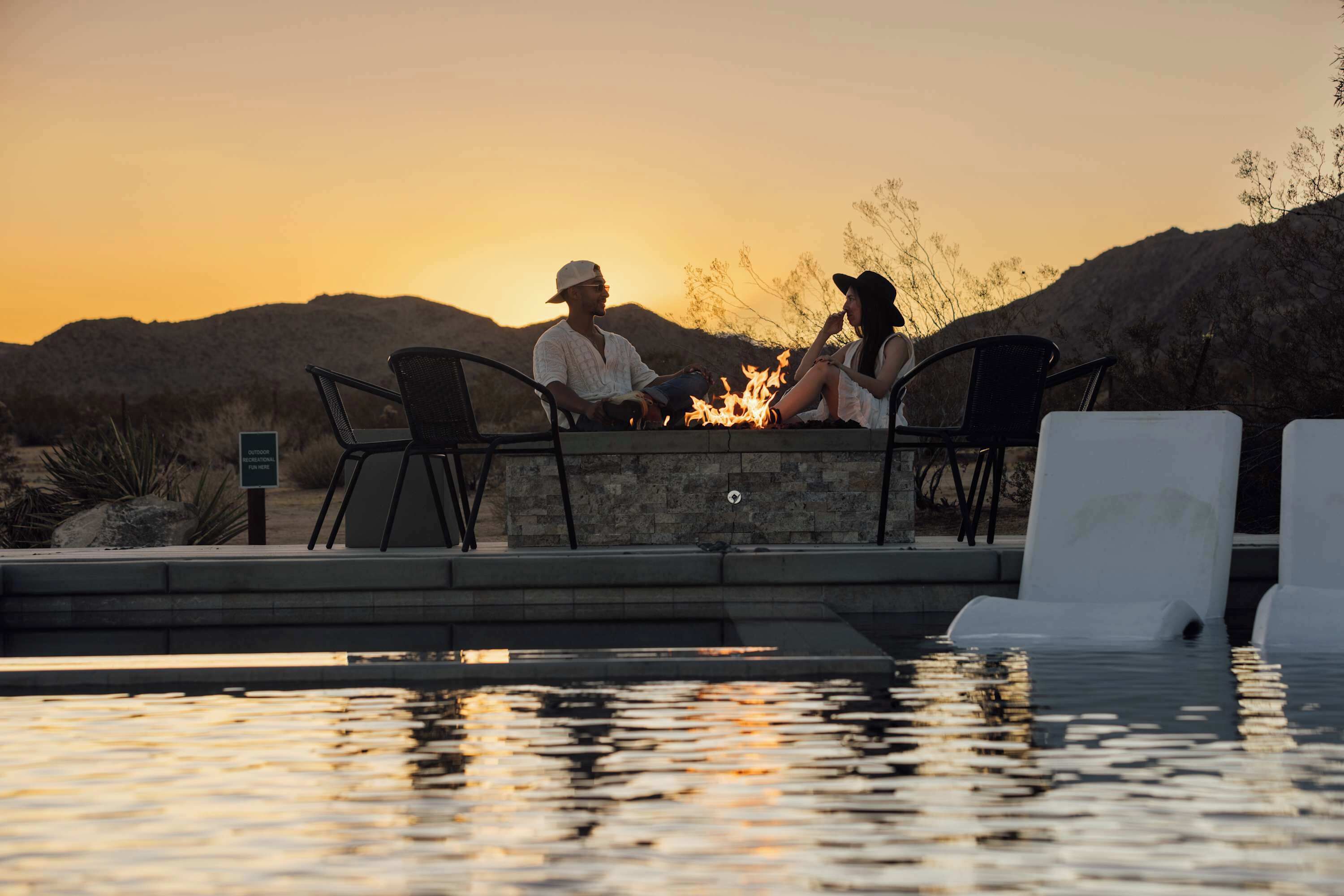 Ein Paar sitzt am Pool, im Hintergrund ein Sonnenuntergang.