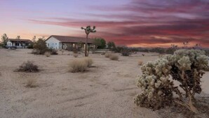 A desert landscape with sparse vegetation, a building with a flat roof, and a clear sky. - Sunflower - 40 Acres, Pool, Pickleball, Game Room! (Joshua Tree)