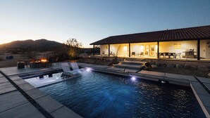 A swimming pool with lounge chairs, a fire pit, and a building with outdoor seating. - Sunflower - 40 Acres, Pool, Pickleball, Game Room! (Joshua Tree)