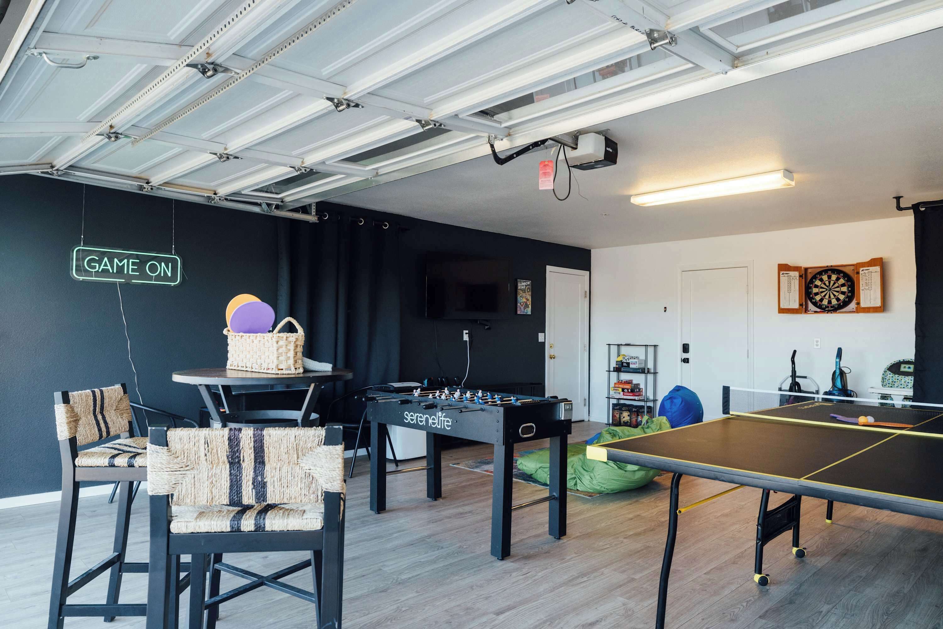 A room with a foosball table, ping pong table, and a dartboard.