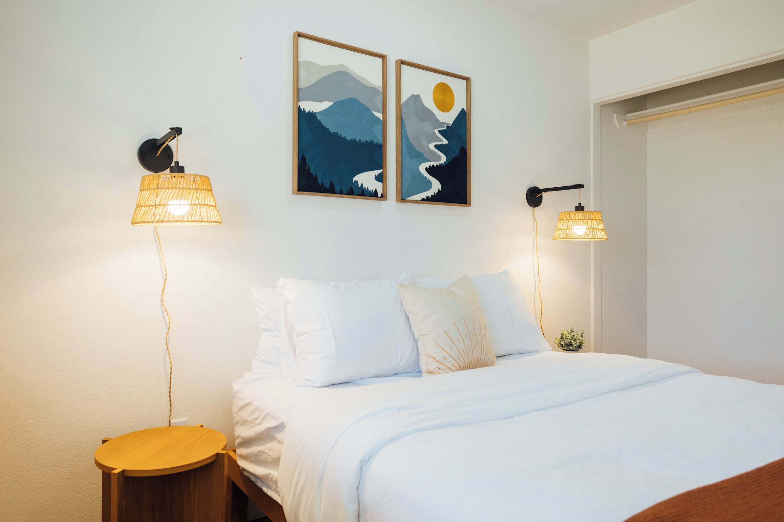 A bedroom with a bed, two wall-mounted lamps, and two framed pictures.