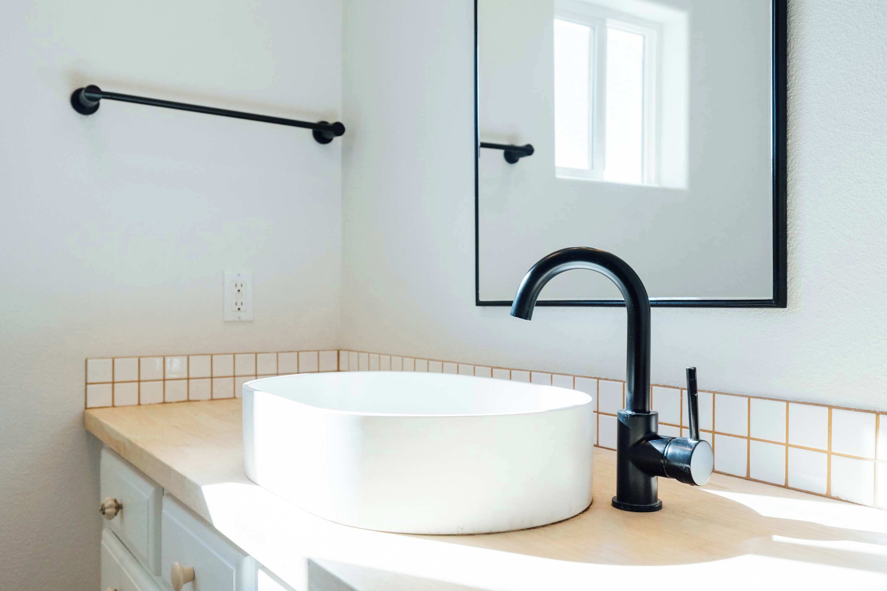 A bathroom with a white sink, black faucet, and a mirror.