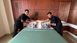 Two individuals adjusting a bed in a room with a wooden panel wall. - Heiwa by Hodo stays (HSR layout)