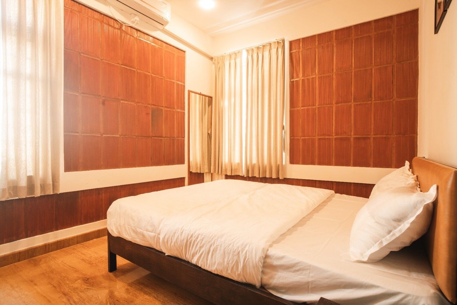 A bedroom with a wooden headboard, a bed with white bedding, and a window with curtains.