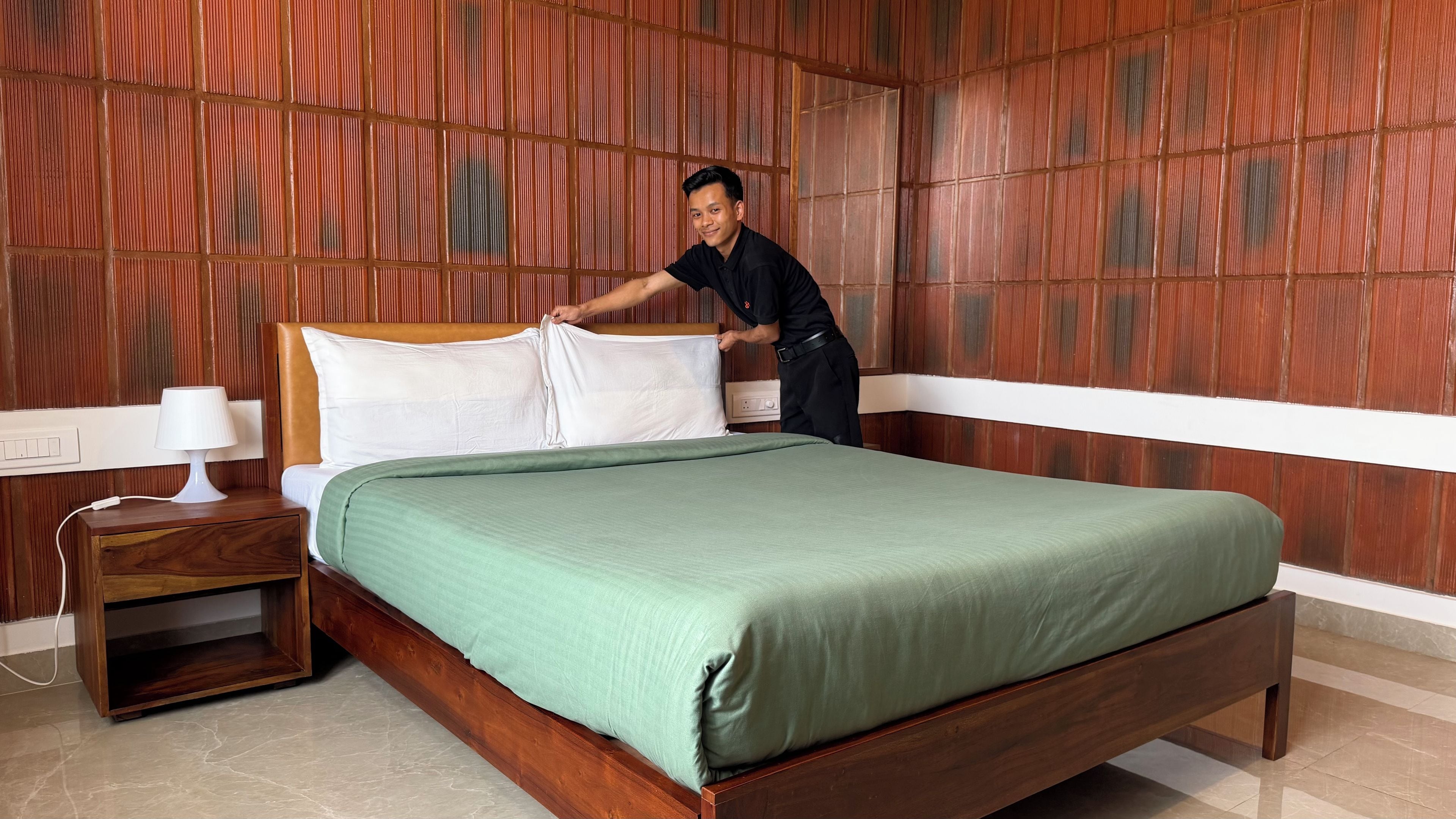 A neatly made bed with a green bedspread and white pillows in a room with wooden paneling on the walls.