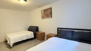 Une chambre avec deux lits, une table de chevet, une petite commode en bois et un luminaire au plafond.