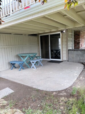 Un patio couvert avec une table et des bancs, une porte-fenêtre coulissante et un mur en briques.