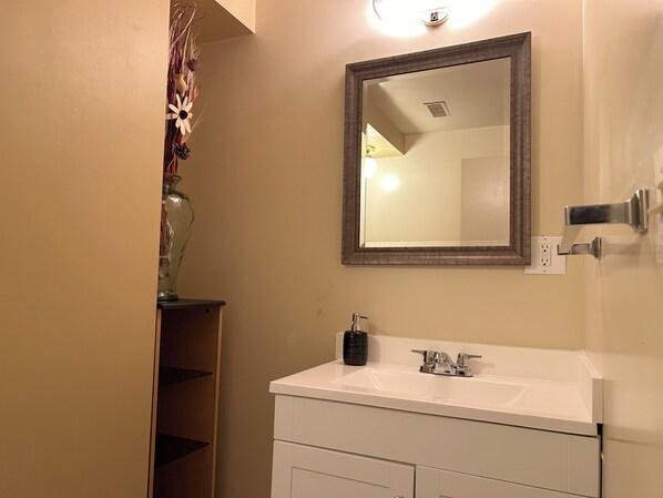 Un baño con un lavamanos blanco, un espejo y un jarrón con flores secas.