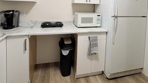 Une cuisine de taille réduite, dotée de meubles blancs, d’un four à micro-ondes, d’une machine à café et d’une poubelle.