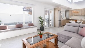 Ein modernes Wohnzimmer mit einem Glastisch, einem grauen Sofa und Meerblick durch große Fenster.