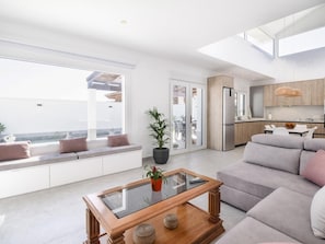 Ein modernes Wohnzimmer mit einem Glastisch, einem grauen Sofa und Meerblick durch große Fenster.