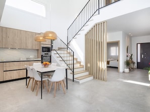 Eine moderne Küche mit Essbereich, einer Treppe und einem Wohnbereich mit Sofa und Pflanze.