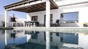 Ein moderner Poolbereich im Freien mit einer Pergola, Sitzgelegenheiten und einem Grill.