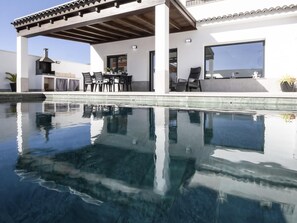Ein moderner Poolbereich im Freien mit einer Pergola, Sitzgelegenheiten und einem Grill.