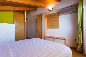 Ein Schlafzimmer mit einem Bett, Holzbalkendecke, einer Wandleuchte, einem Fenster und einem grünen Vorhang.