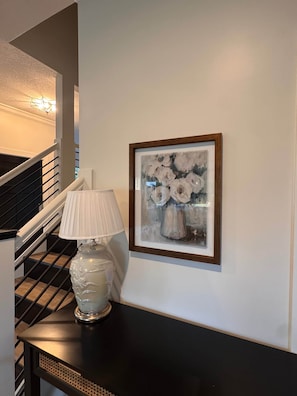 Uma escadaria com corrimão preto, parede branca e um quadro emoldurado com flores.