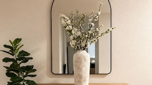 Ett konsolbord i trä med en vas med vita blommor och en spegel ovanför.