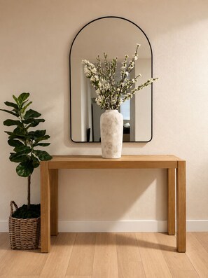 Ein Holzkonsolentisch mit einer Blumenvase und einem Spiegel darüber.
