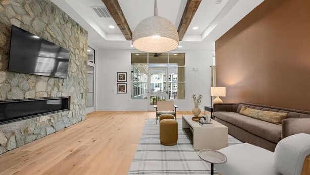 Un salon moderne avec un mur en pierre, un plancher en bois, un téléviseur à écran plat, un canapé, des poufs et une table basse.