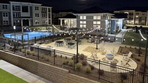 Une vue nocturne d’un immeuble résidentiel doté d’une piscine, d’un espace extérieur aménagé avec des sièges et d’une terrasse bien éclairée.