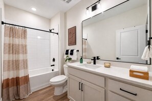 A modern bathroom with a bathtub, toilet, and vanity with a mirror. - 2 King Beds | Pool, Gym & Easy First-Floor Access (Mooresville)