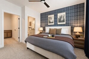A bedroom with a bed, bedside tables, a ceiling fan, a bathroom with a toilet and sink, and a hallway.