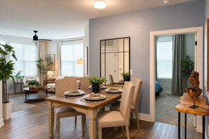 A dining area with a wooden table, beige chairs, and potted plants. - 2 King Beds | Pool, Gym & Easy First-Floor Access (Mooresville)